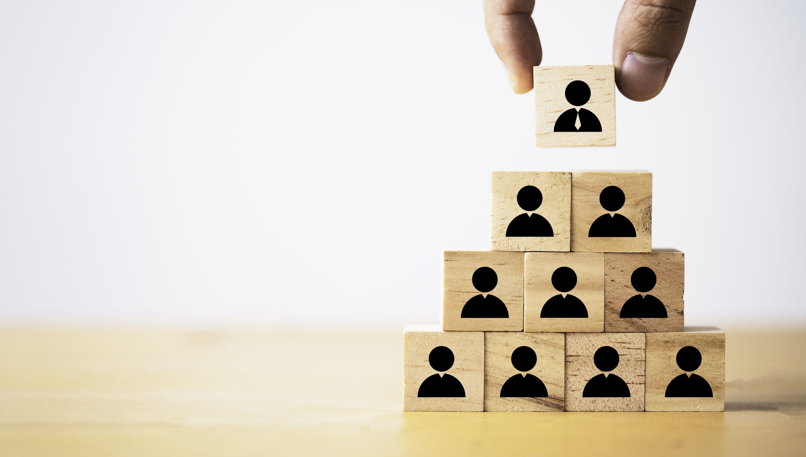 Hand stacking wooden blocks with human icons in a pyramid, symbolising building security awareness in organisations.