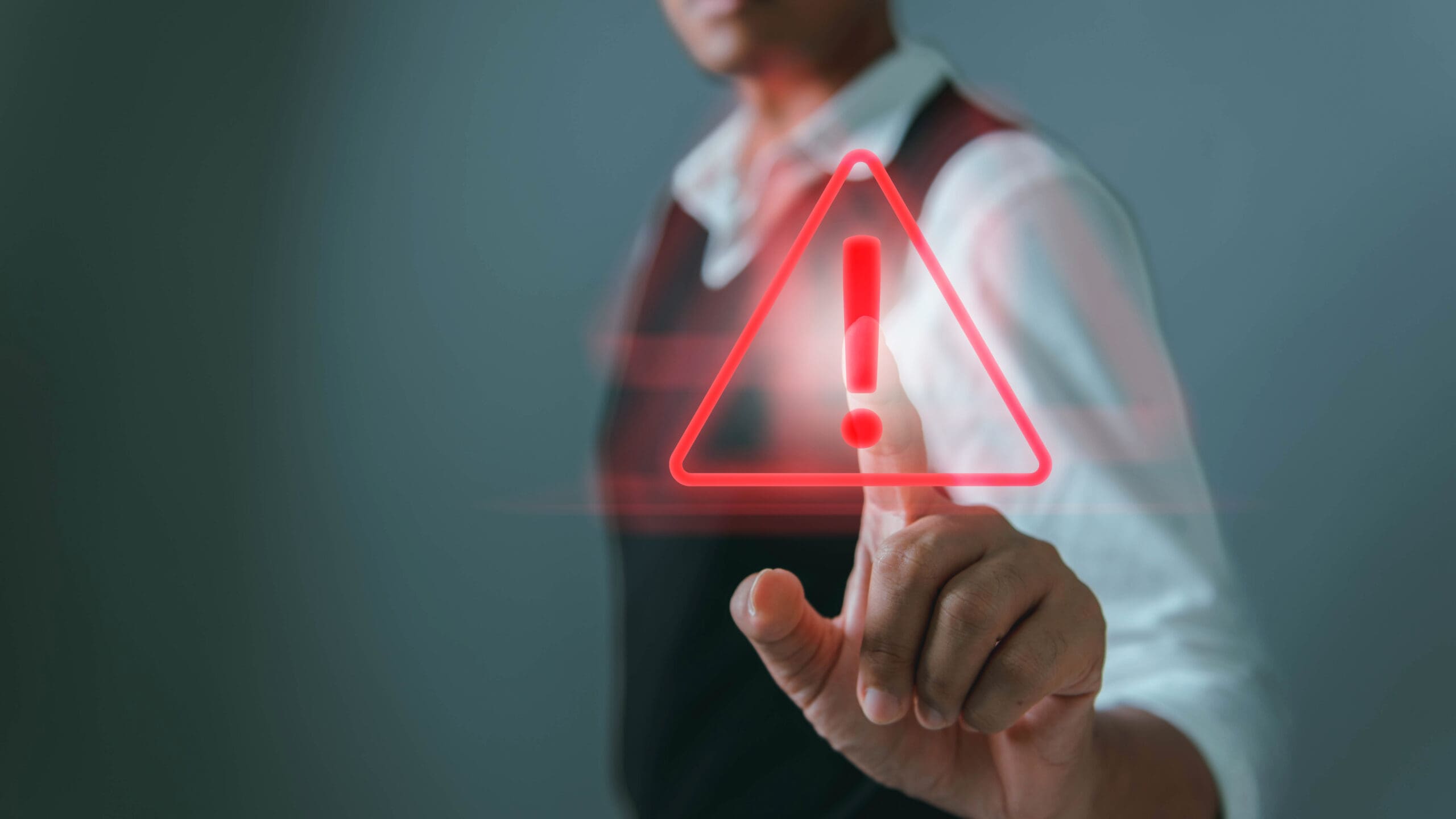 Data breach alert concept — visualising cybersecurity risk detection. Person pressing a red digital warning icon representing a data breach or cybersecurity alert.
