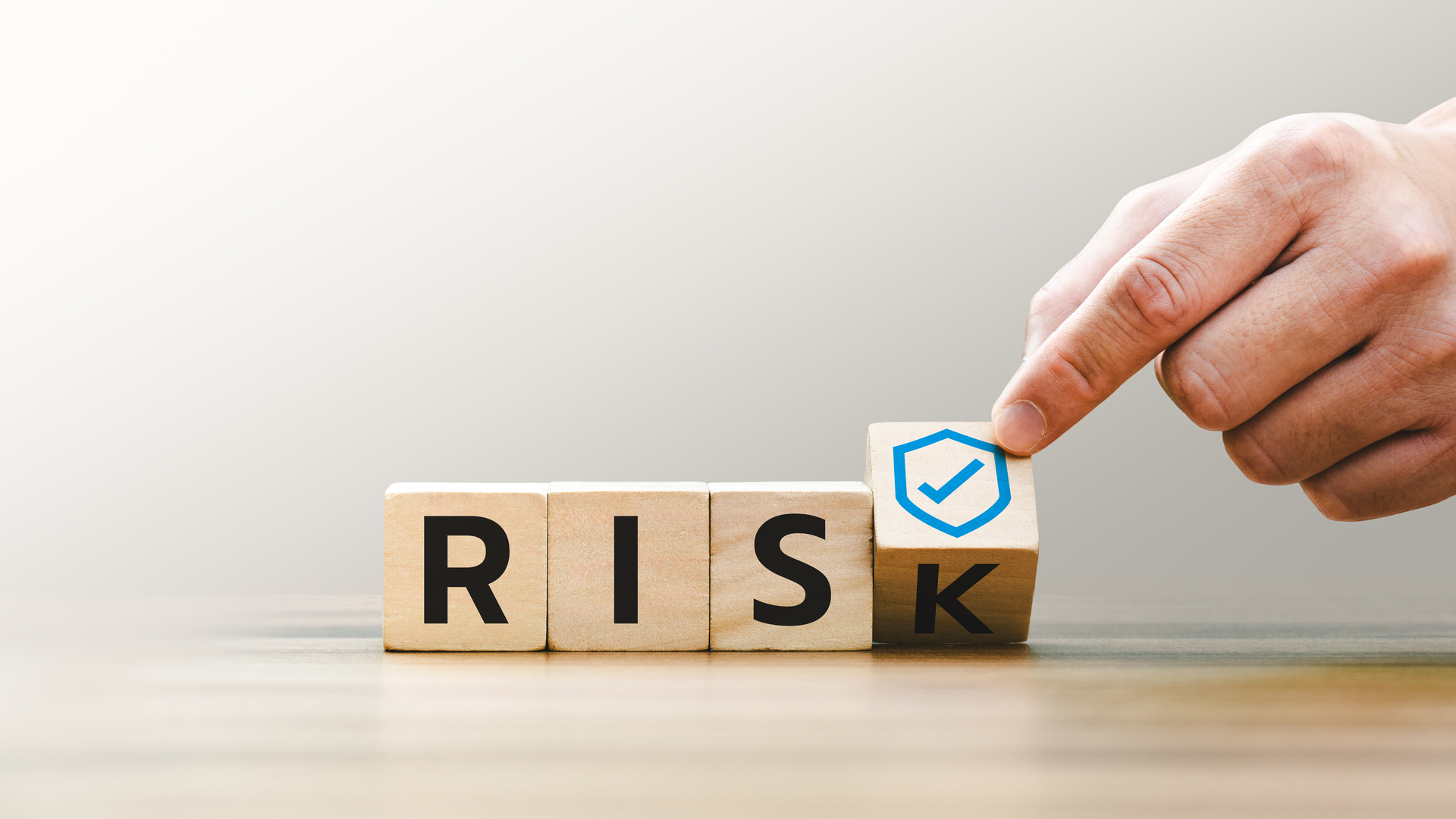 Hand placing a checkmarked block next to the word “Risk”, representing cybersecurity risk management and executive decision-making