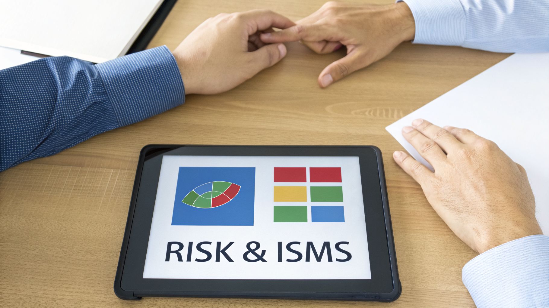 Two professionals reviewing risk management and ISMS information on a tablet at a wooden desk.